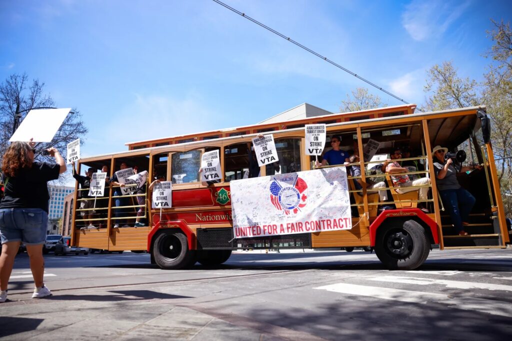A picture of a historic trolly with VTA strike banners and union workers carrying signs